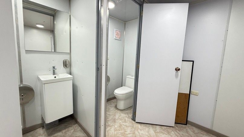 Bathroom module with a sink and vanity, a mirror, soap and paper dispensers, and a toilet stall.