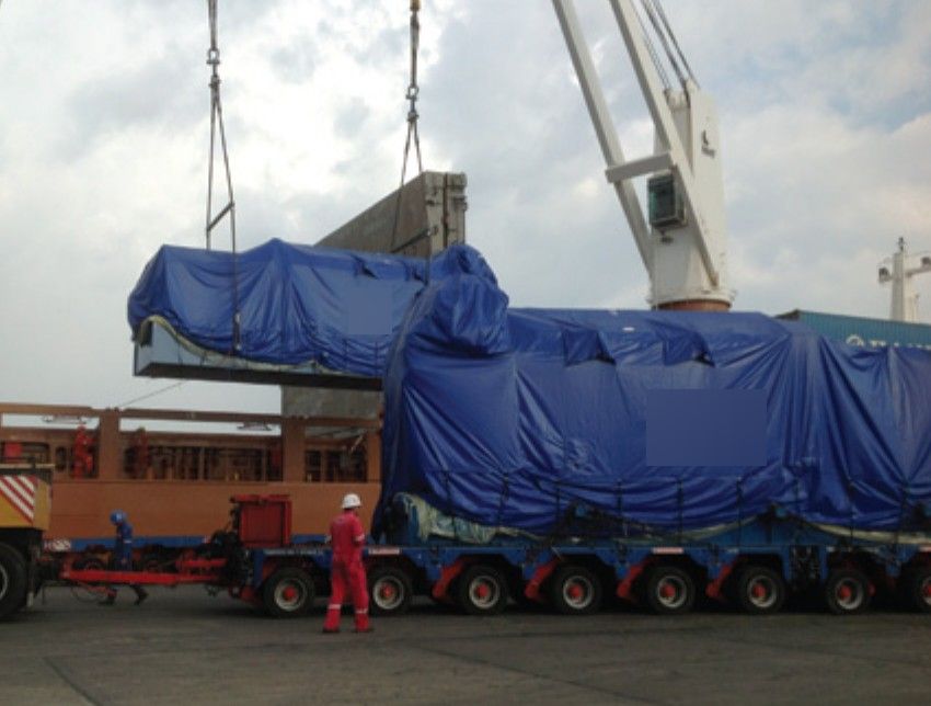 Transport of a tarp-covered piece of equipment on a multi-axle modular platform, with a lifting maneuver.