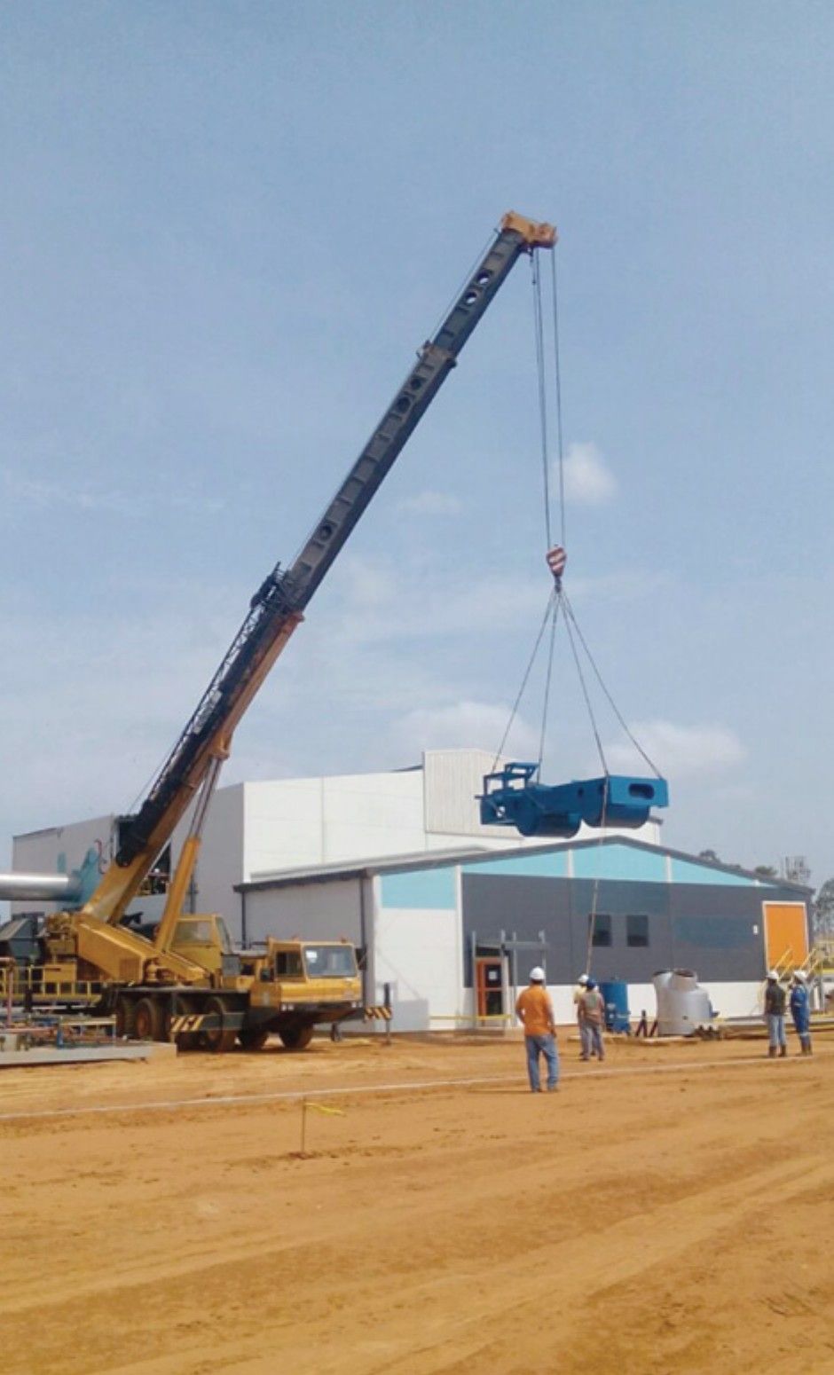 Mobile crane lifting a heavy blue piece of equipment next to the plant building during assembly.
