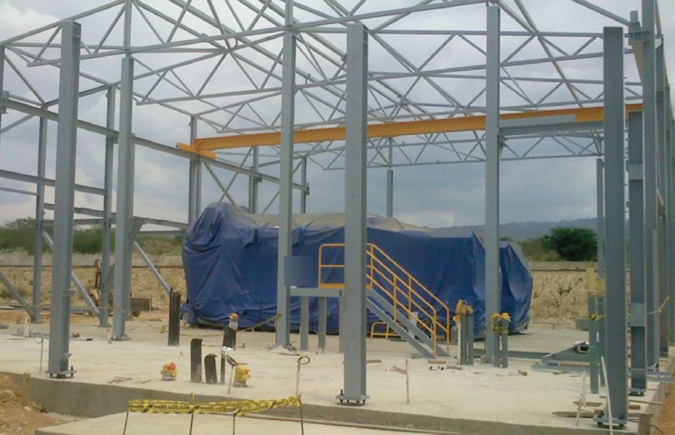 Trujillo plant: steel structure of the engine hall under construction, with an engine generator covered by a blue tarp and a staircase with yellow railings.